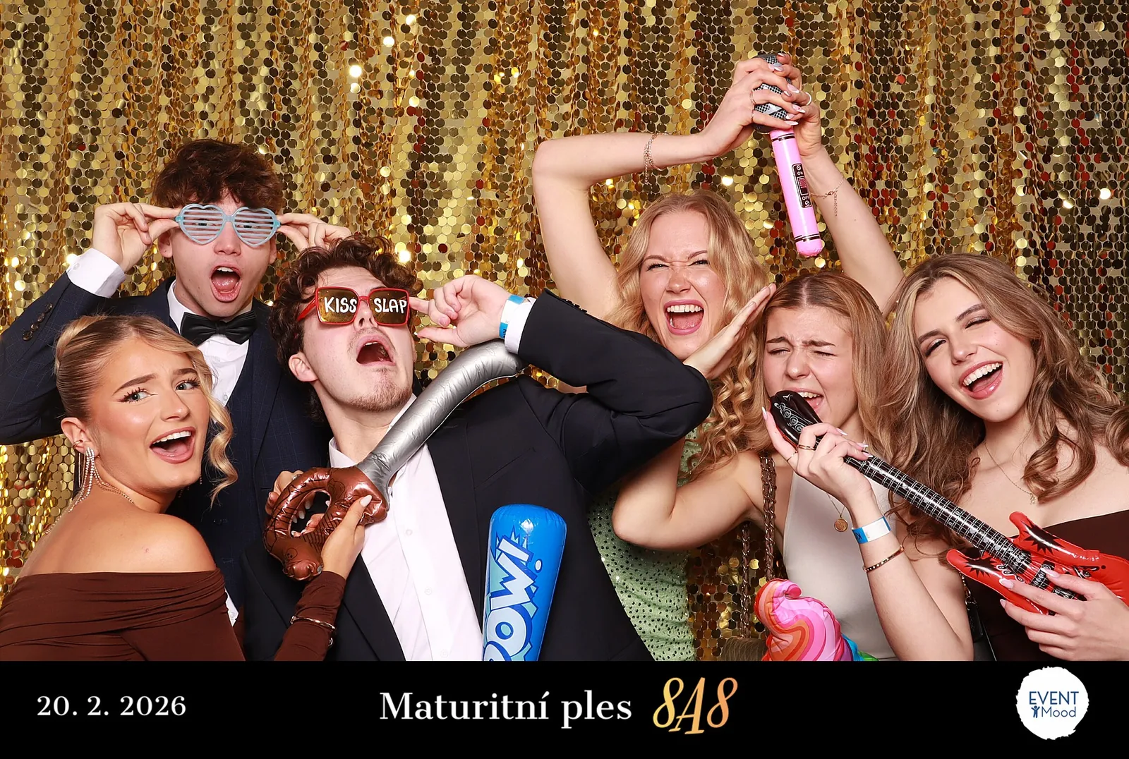 Skupina maturantů s rekvizitami před zlatým pozadím fotokoutku